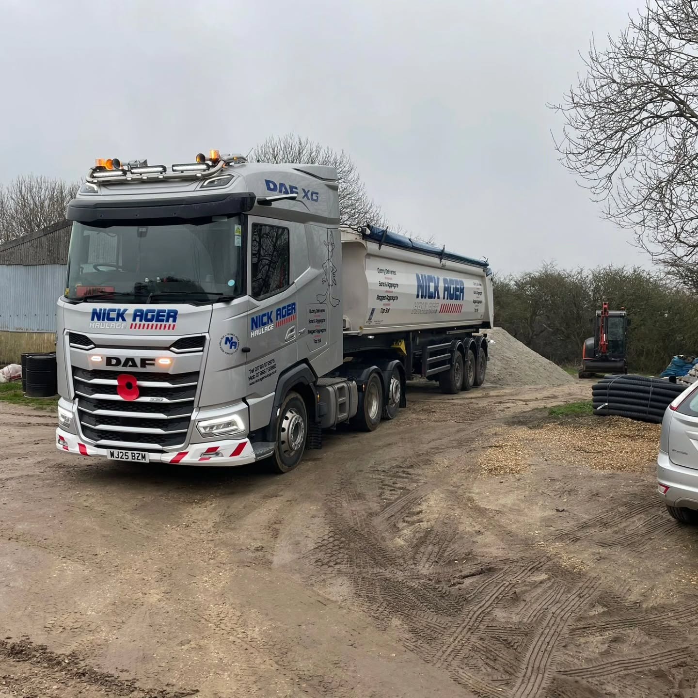 A DAF XG truck belonging to Nick Ager Haulage is parked on a gravel surface with a trailer loaded with raw materials. In the background, a small excavator and storage items are visible.