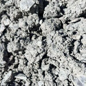 A close-up view of a grey cement mix with a rough, uneven texture, showcasing small lumps and particles.