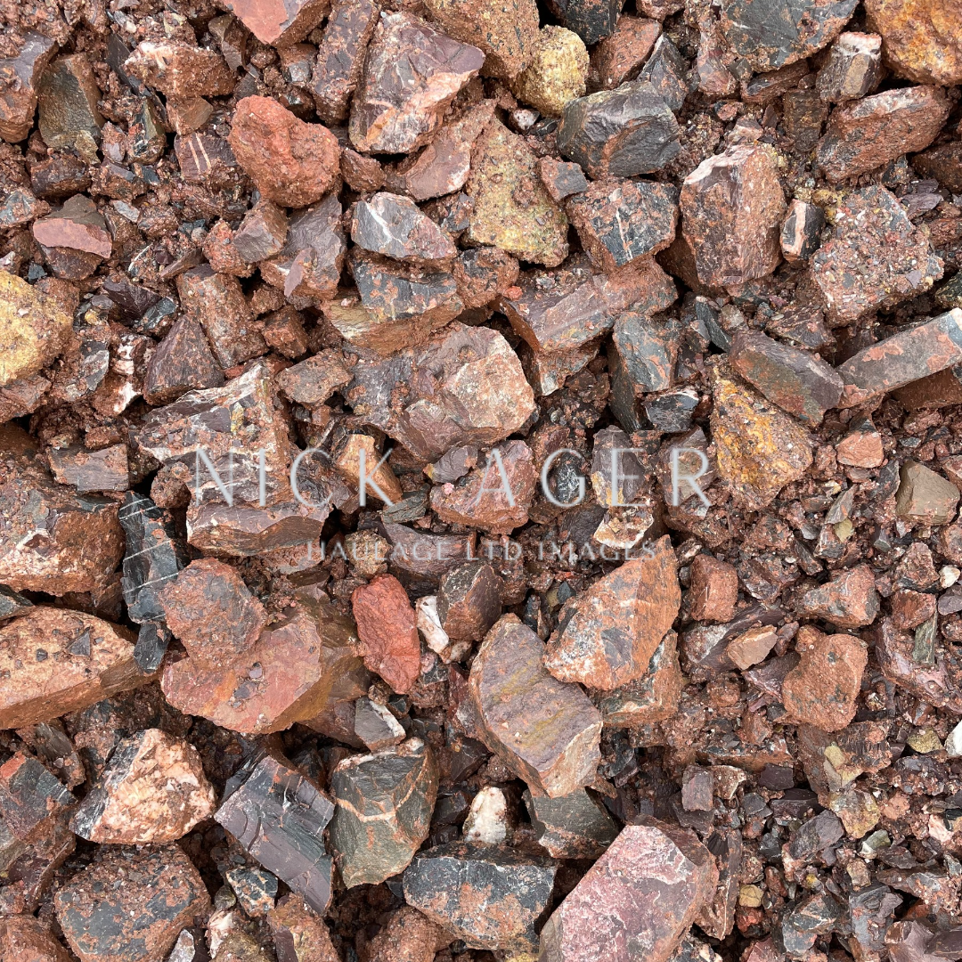 A close-up view of an assortment of textured rocks in various shades of brown, red, and grey, showcasing their jagged edges and surface details.