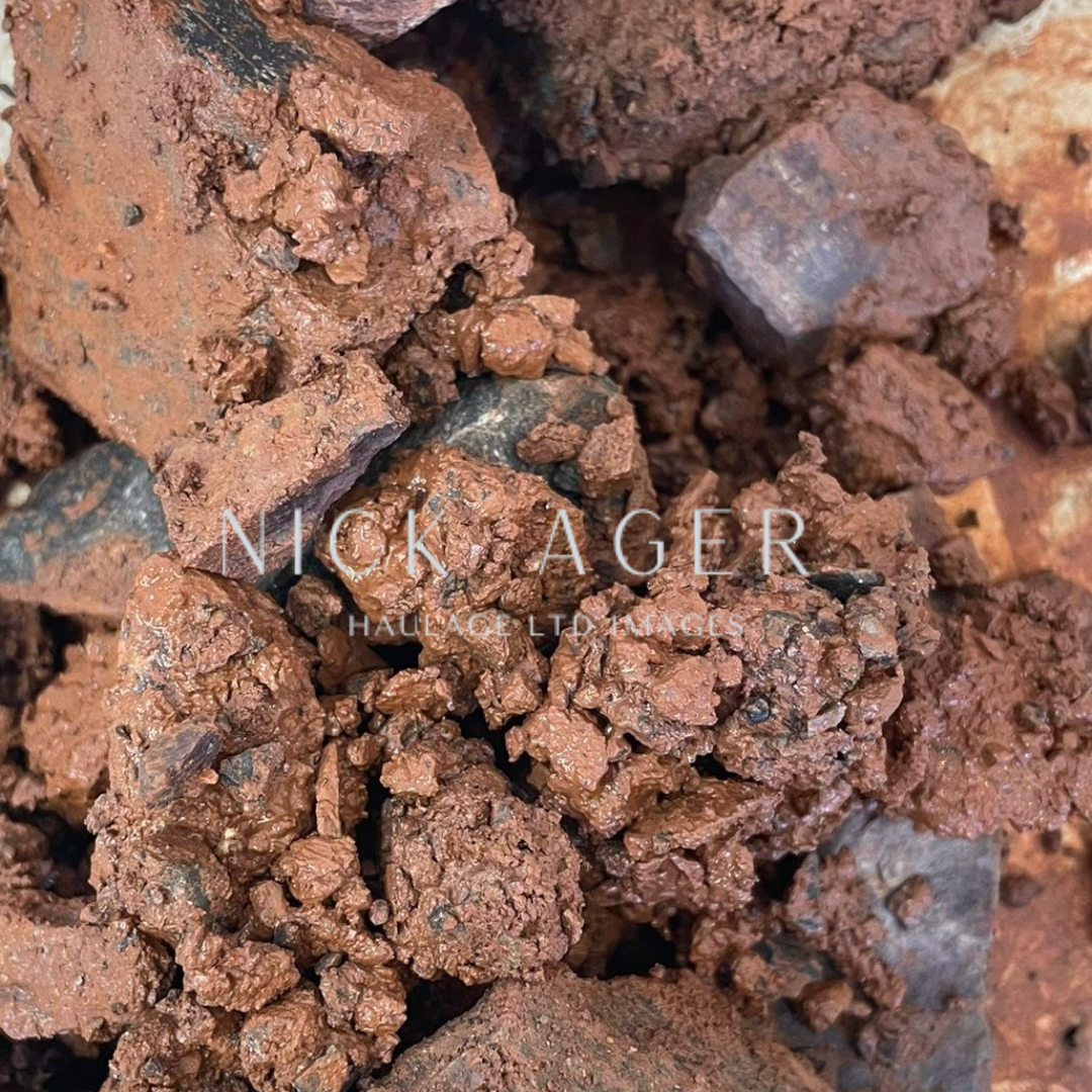 A detailed image of reddish-brown mineral aggregates with a rough texture and varying sizes of pieces, some darker in shade, on a surface.