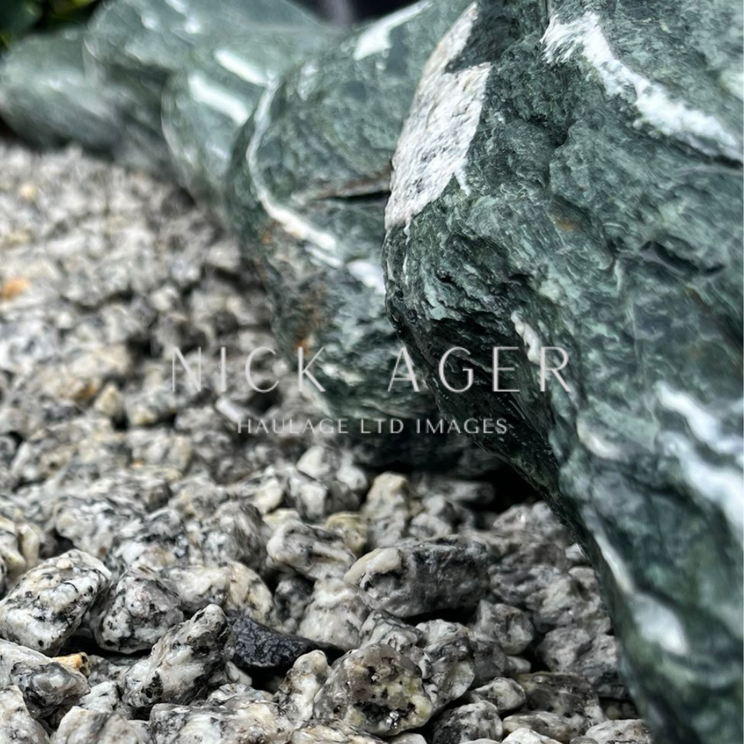 A close-up view of a green stone resting on a bed of grey gravel, showcasing the texture and colours of both the stone and the gravel.