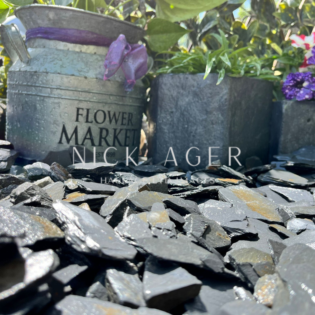 Metal flower market bucket and stone planters surrounded by slate gravel in a garden setting