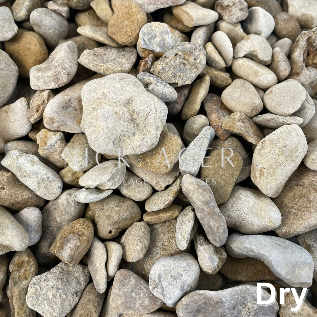 A close-up view of various dry decorative pebbles in shades of grey and tan, featuring smooth surfaces and varying shapes.