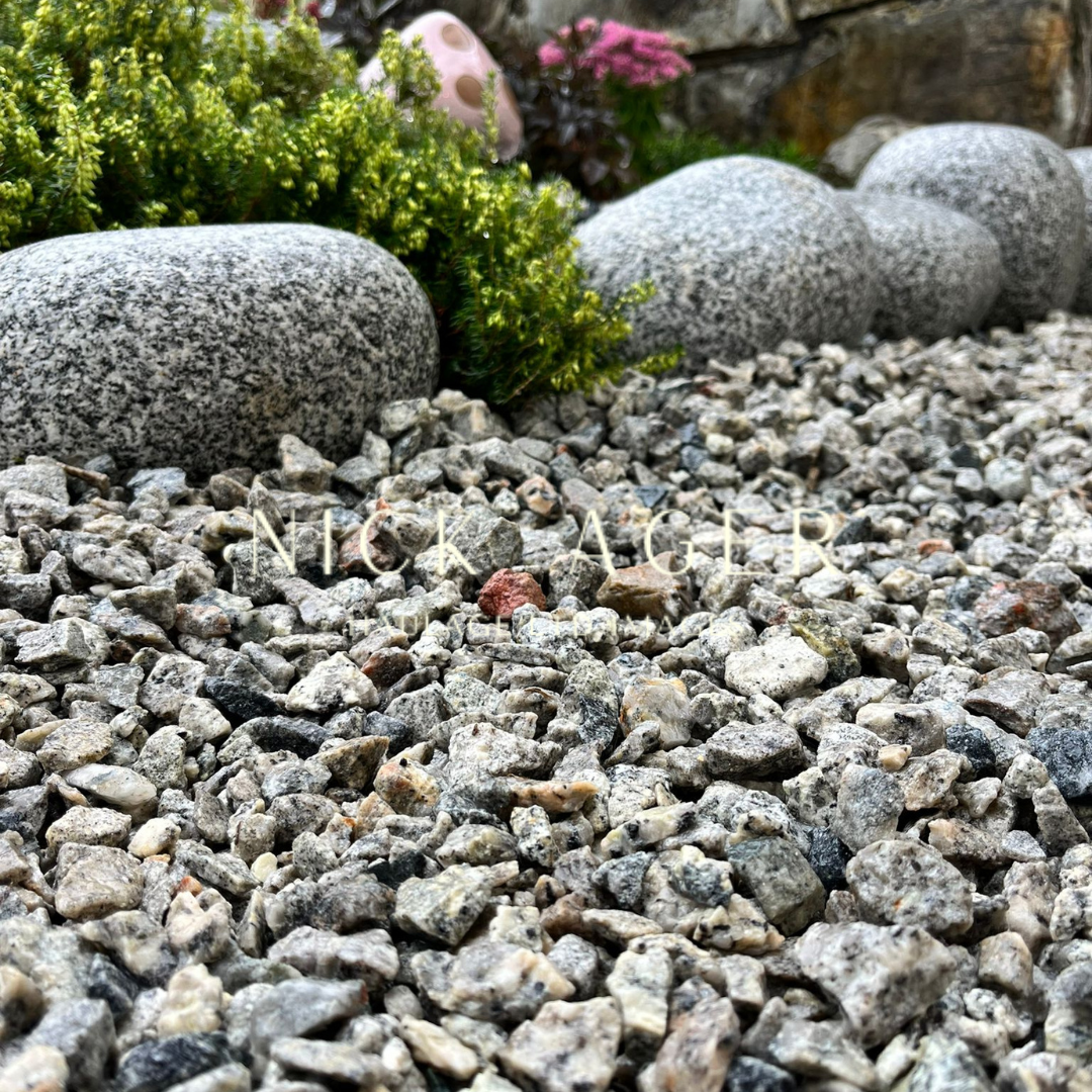 A close-up view of gravel stones on a garden path, with larger decorative stones and greenery in the background, creating a serene outdoor setting.