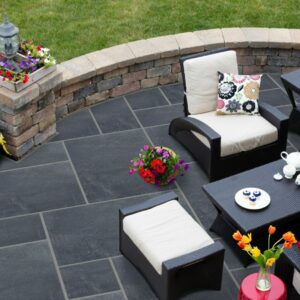 A beautifully arranged outdoor patio featuring wicker chairs, a coffee table with tea and pastries, and vibrant flower pots.