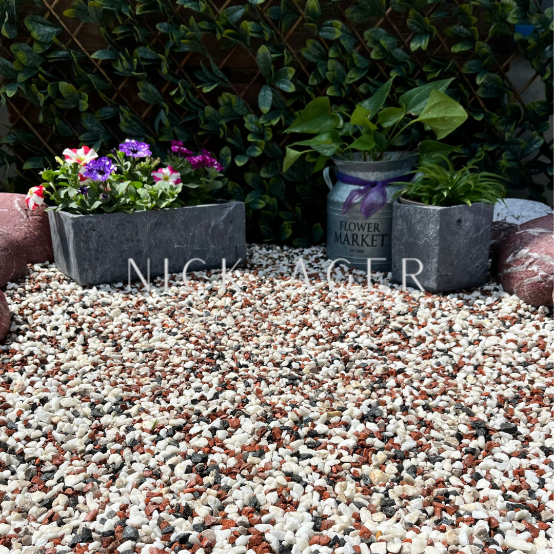 A vibrant garden scene featuring colourful flowers in a grey planter, a decorative tin marked 'Flower Market', and a variety of decorative stones on the ground.