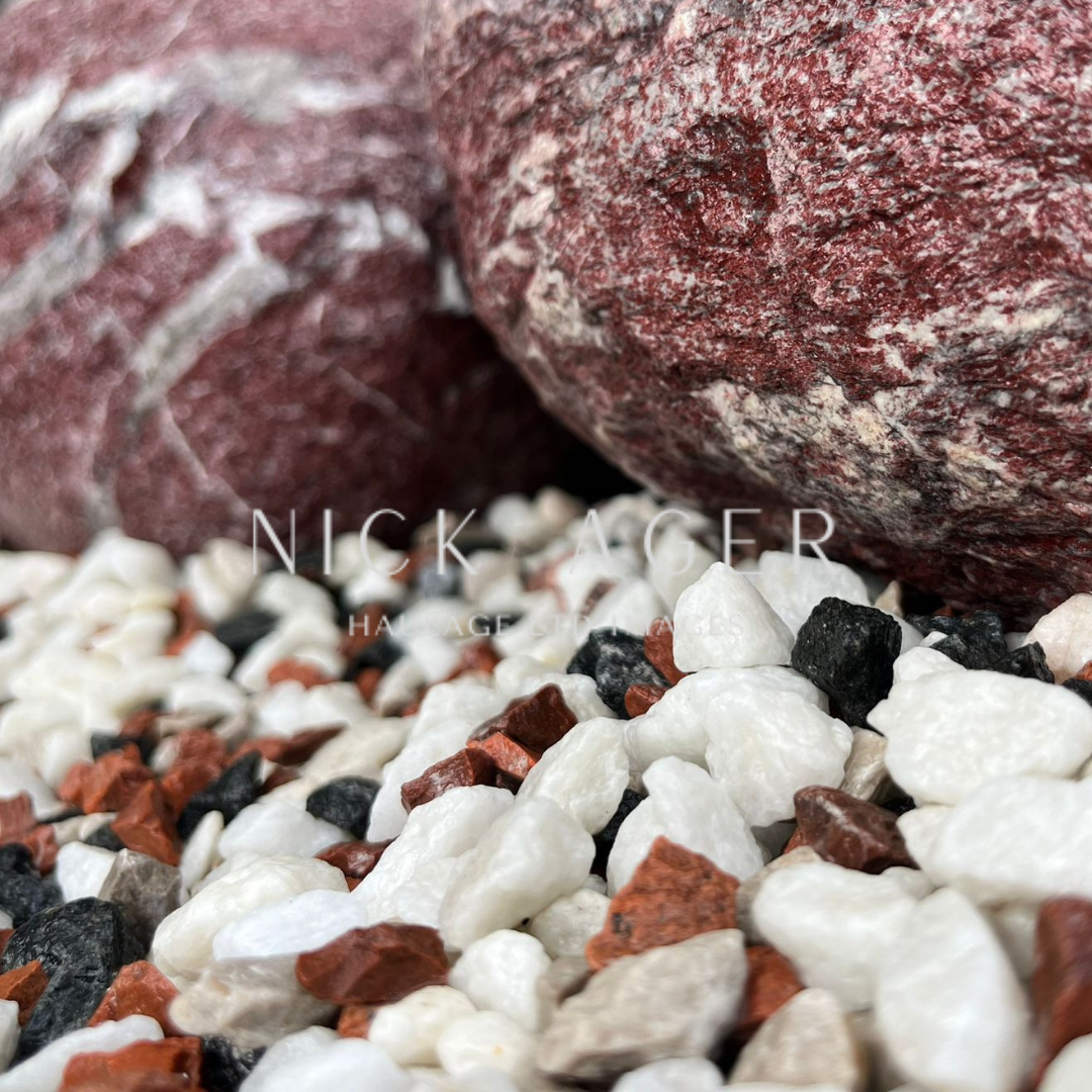 A close-up view of various decorative stones, featuring red, black, and white pebbles with larger red marble rocks in the background.