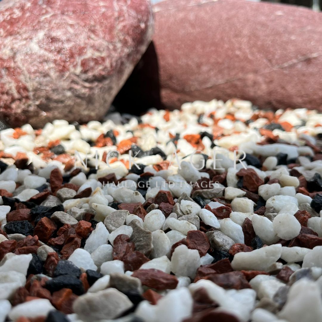 Close-up view of a variety of small gravel stones in shades of white, red, and black, with larger reddish stones in the background.