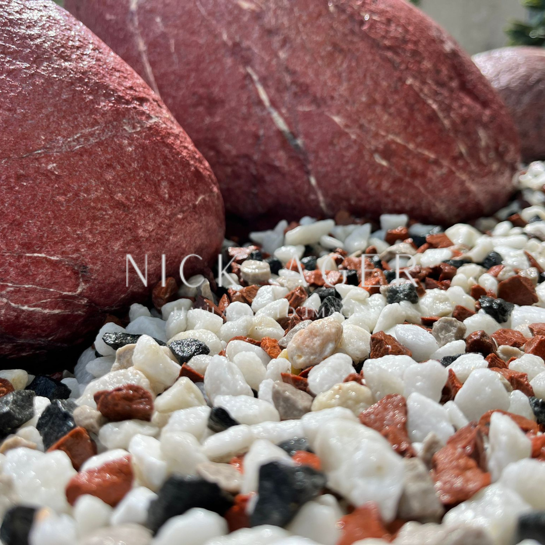 Close-up of polished red stones resting on a bed of small, colourful gravel, including white, black, and reddish stones.