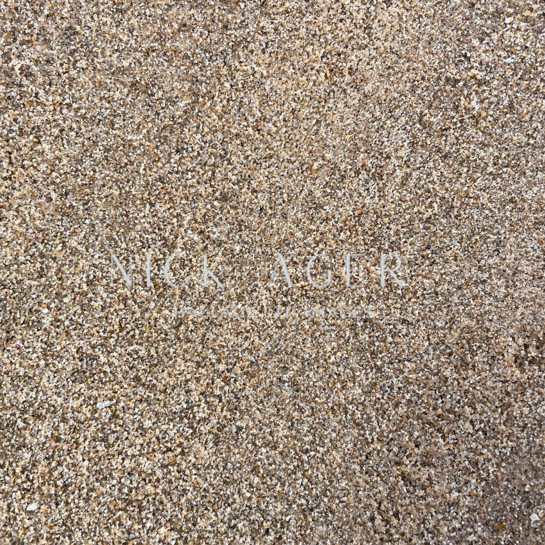 A detailed view of sand displaying a variety of small grains in shades of brown and beige.