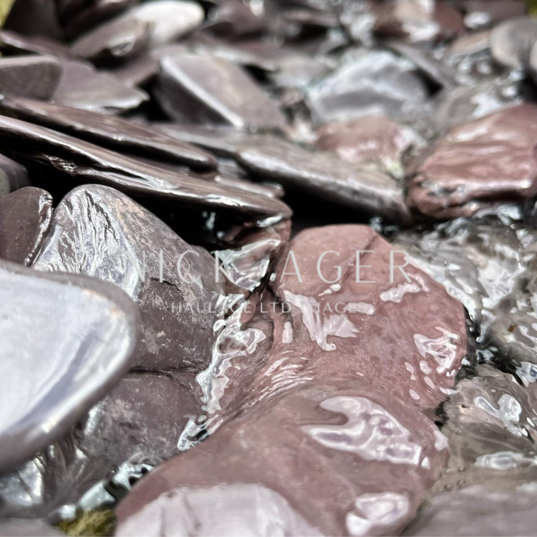 A close-up view of smooth, glossy pebbles in varying shades of purple and grey, partially covered in water.