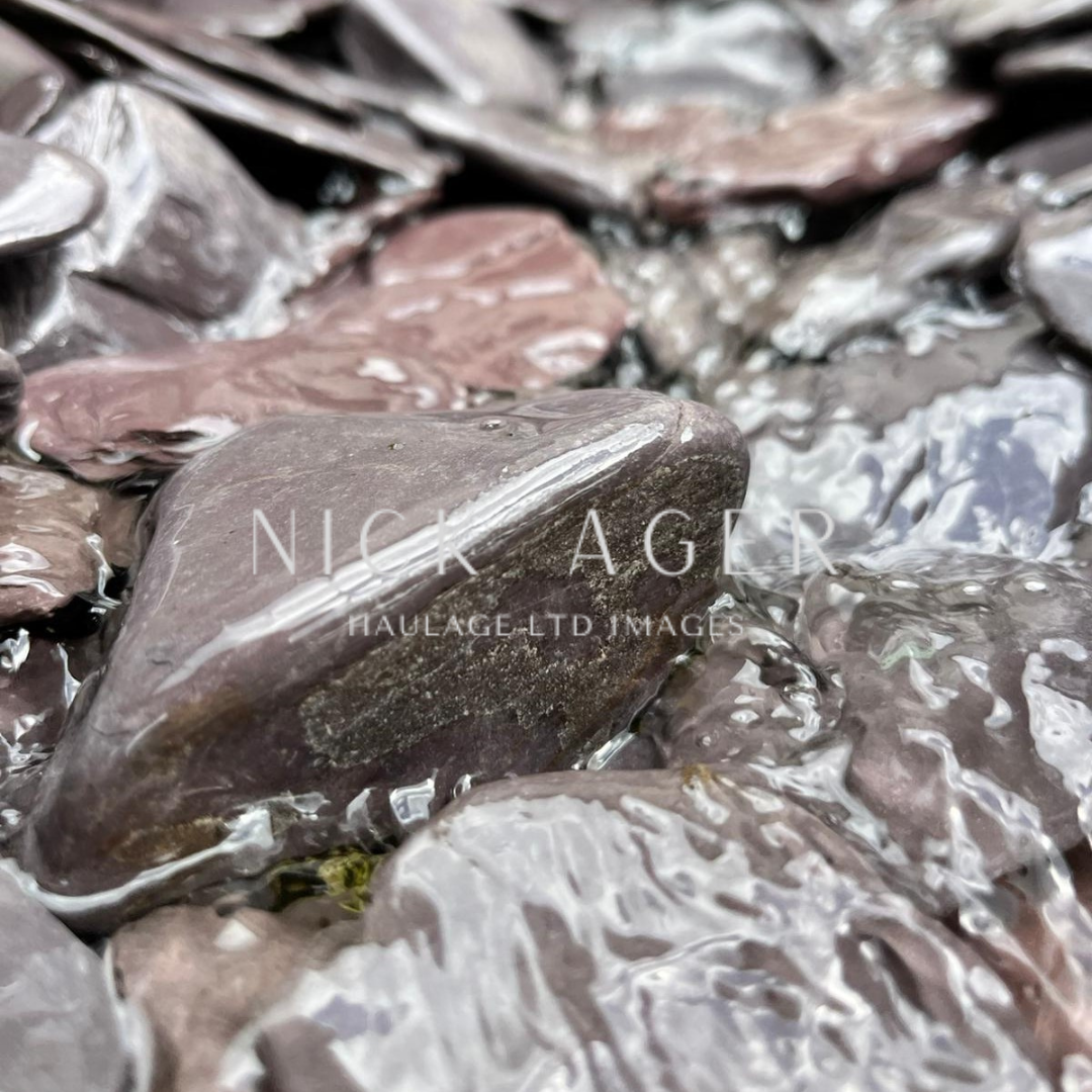 A close-up view of smooth, dark stones partially submerged in clear water, creating a tranquil, reflective surface.
