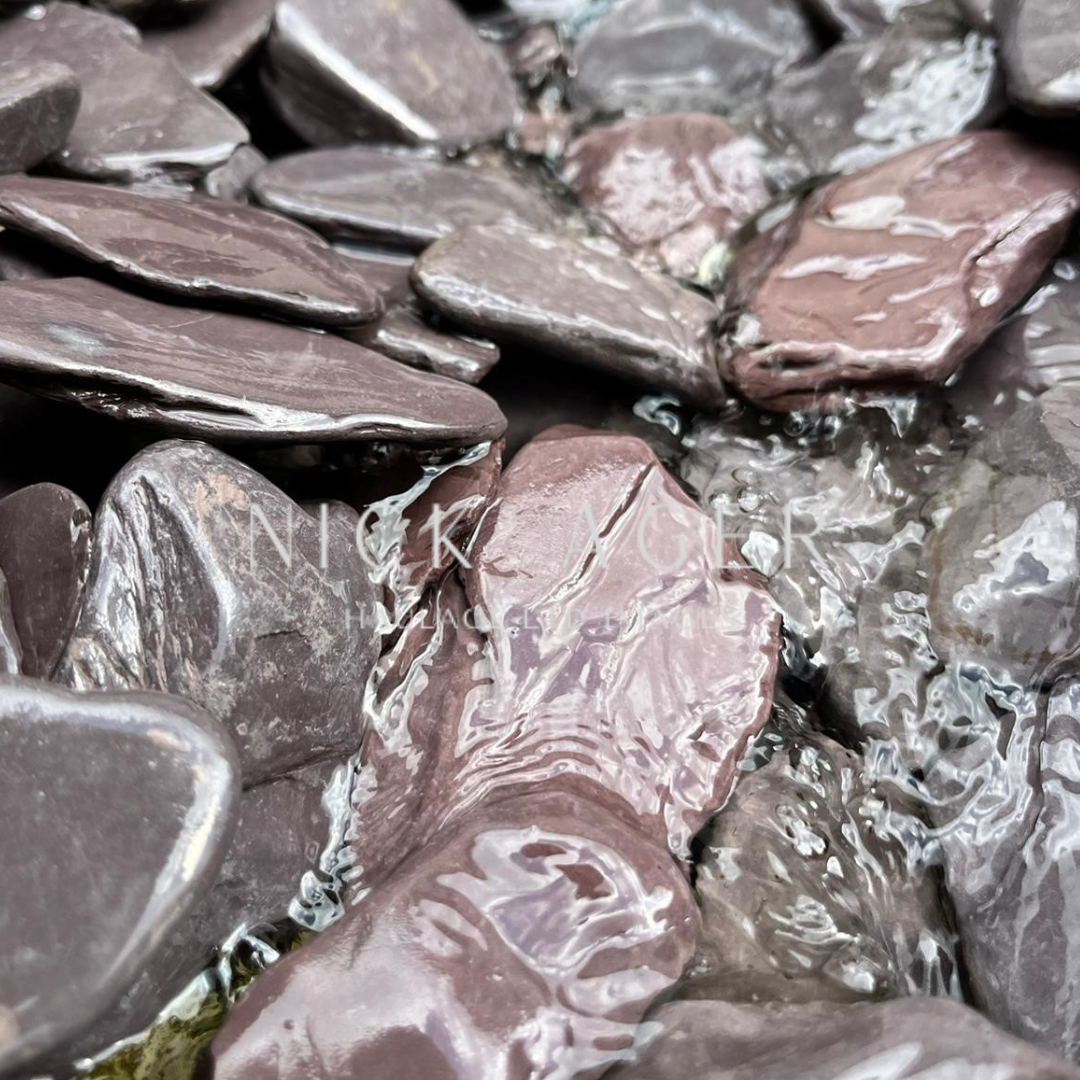 A close-up view of smooth, rounded purple stones submerged in clear water, showcasing their glossy surface and unique textures.