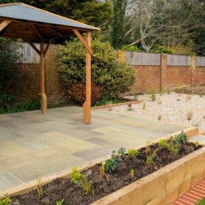 A beautifully designed garden featuring a wooden gazebo on a stone patio, surrounded by landscaped areas with plants and gravel.
