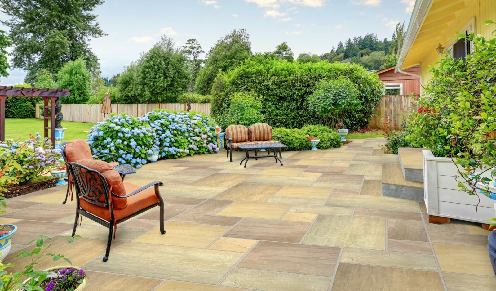 A landscaped patio featuring a stone floor, comfortable seating, and vibrant hydrangea bushes in the background.