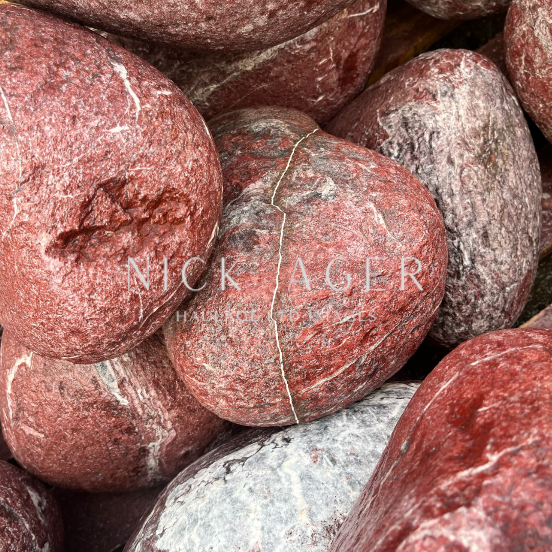 A close-up image of a pile of rounded red stones with varying textures and patterns, featuring some grey marbling and visible cracks.