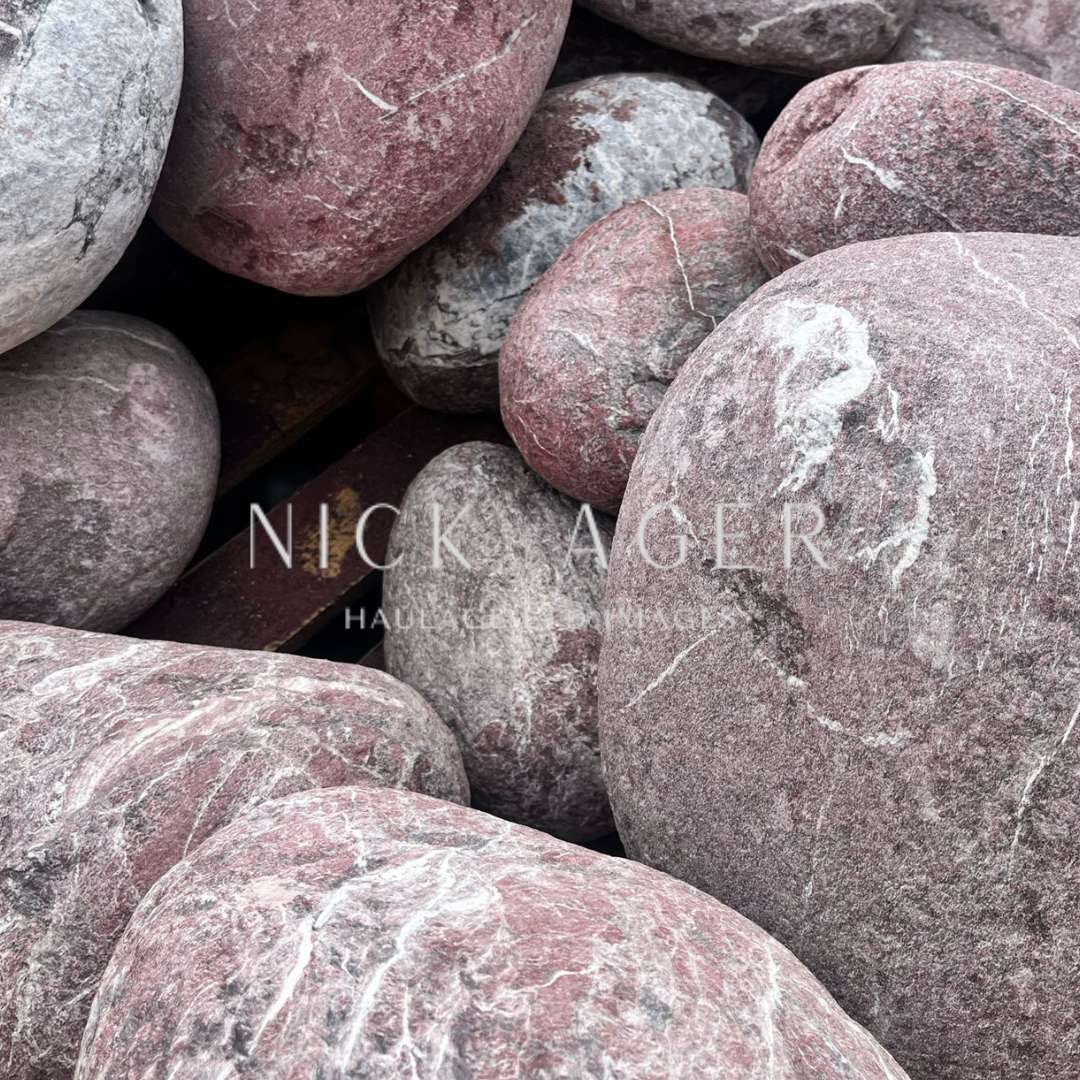 A collection of smooth, round stones in various shades of grey and pink, stacked closely together.