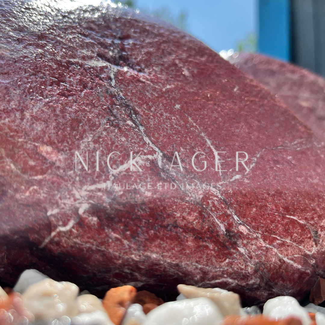 A close-up view of a large red stone featuring prominent white veins, set against a background of smaller pebbles.