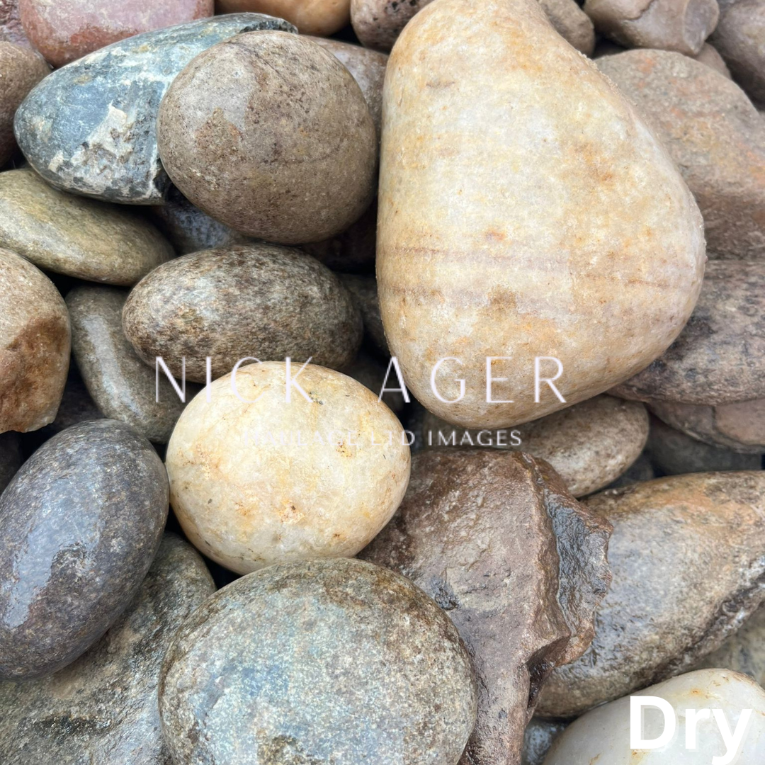 An assortment of smooth, rounded river stones in various shades, including golden, brown, and grey, resting on one another.