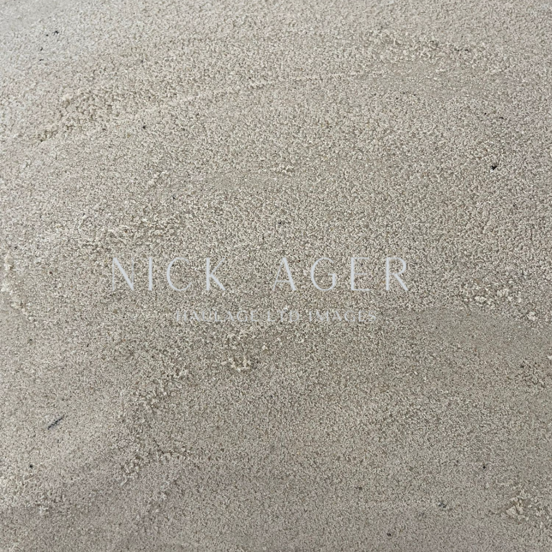 A close-up image of a sandy texture, featuring a light brown surface with fine grains, overlaid with the name 'Nick Ager' in white text.