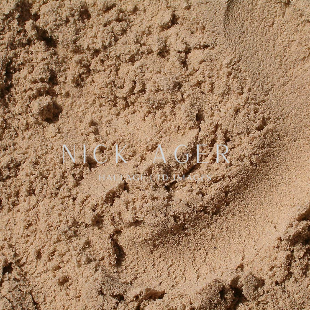 A detailed view of fine sand with a soft texture, displaying various grains and shades of beige, with superimposed text.