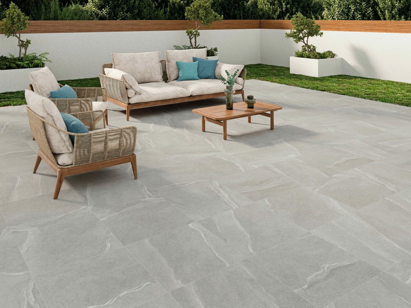 A contemporary outdoor patio featuring a comfortable beige sofa with blue cushions, two matching armchairs, a wooden coffee table, and a green lawn in the background.