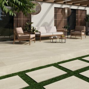 A contemporary outdoor patio featuring light-coloured tile flooring, two wooden chairs, a sofa, and decorative plants under a wooden pergola with hanging pendant lights.