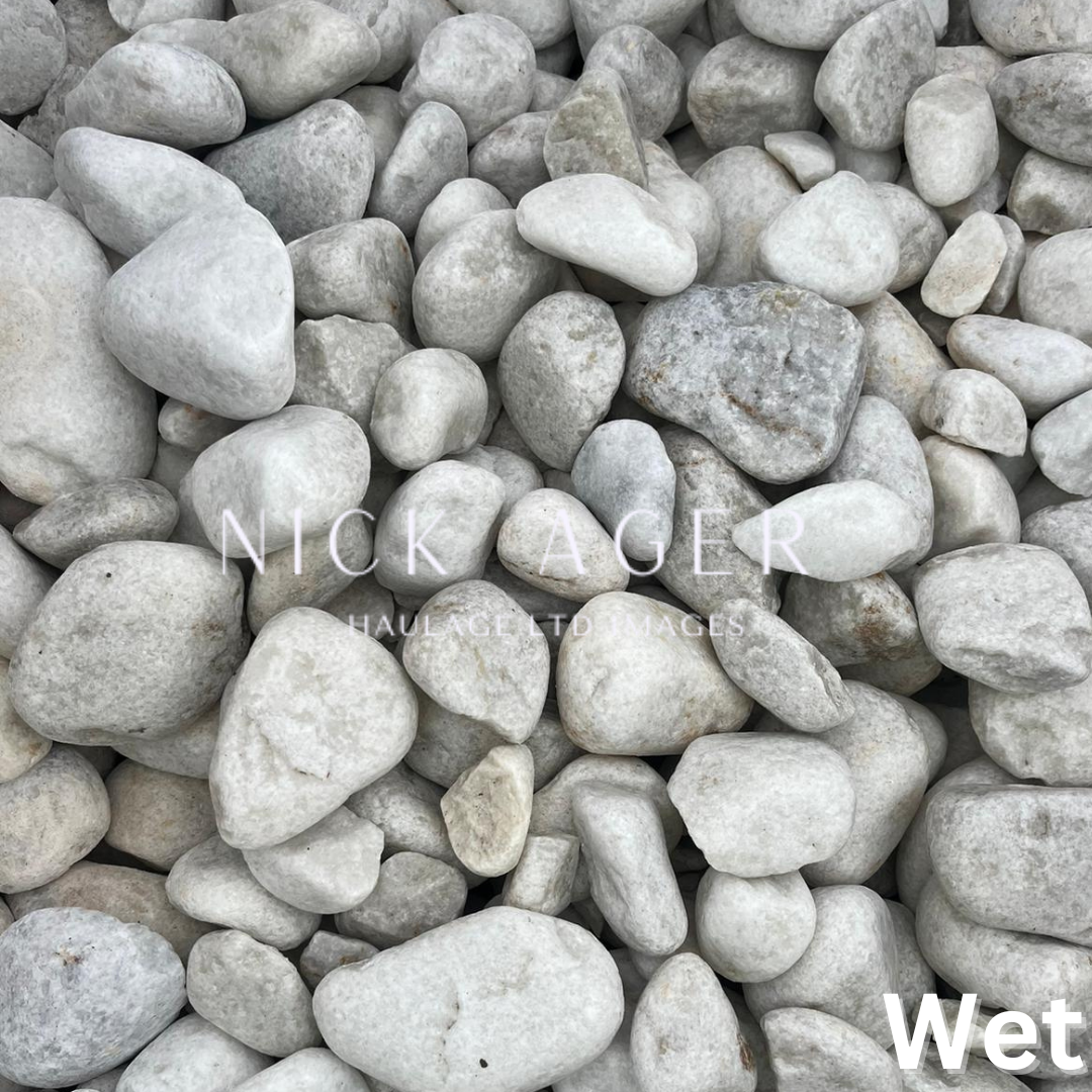 A close-up view of wet white pebbles, showcasing various shapes and sizes, with a smooth surface and a natural greyish hue.