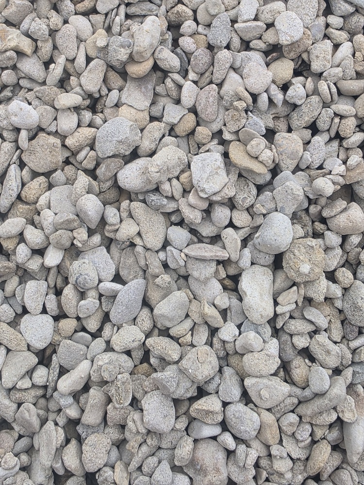 A textured surface of assorted pebbles and gravel stones in shades of grey and beige.