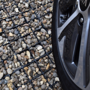 Close-up of a gravel grid system with rounded stones, featuring a car wheel beside it.