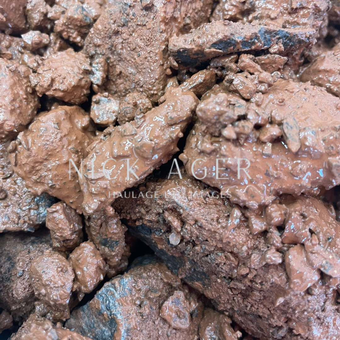 A detailed view of brown clay soil with various chunks and textures, glistening with moisture.
