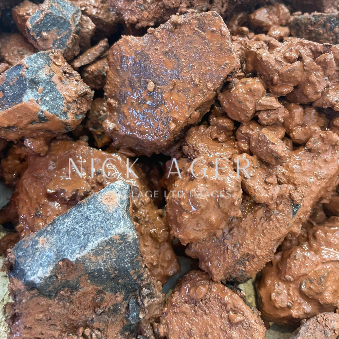 Close-up view of reddish brown iron ore chunks with dark specks, showing a rough and textured surface.